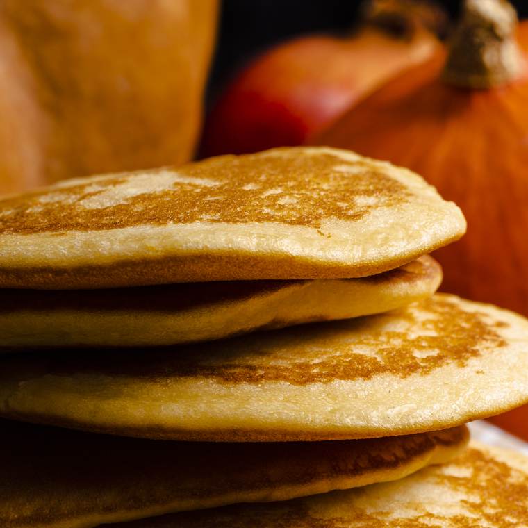 A stack of golden pumpkin pancakes with pumpkins in the background